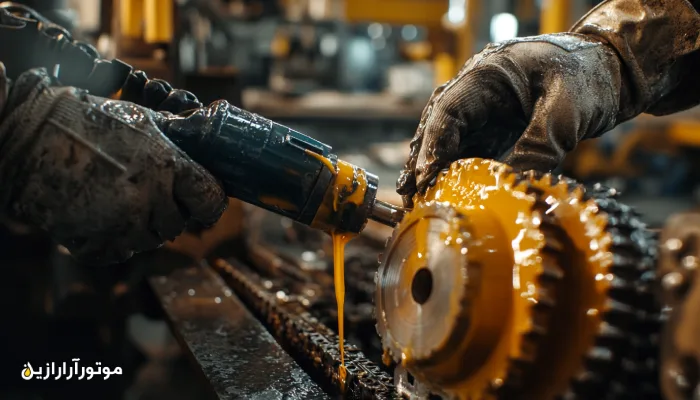 روغن‌کاری زنجیر و چرخ‌دنده صنعتی با استفاده از گریس غلیظ؛ تکنسینی با دستکش ایمنی در حال اجرای فرآیند روانکاری در محیط کارخانه