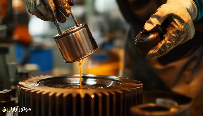 نمای نزدیک از دستکشهای صنعتی در حال اعمال روغن روانکار بر سطح چرخدنده بزرگ با استفاده از ظرف فلزی، در فضای کارگاه تخصصی.