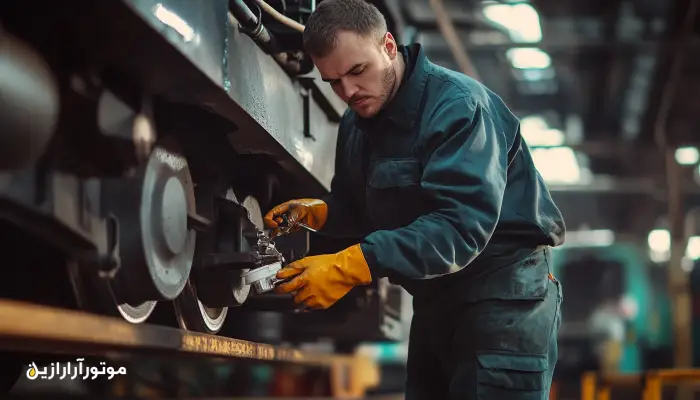 تعمیرکار فنی با دستکش ایمنی در حال سرویس و روغنکاری گیربکس قطار در کارگاه نگهداری، نمای نزدیک از تجهیزات زیرین قطار و اهمیت استفاده از روانکار EP