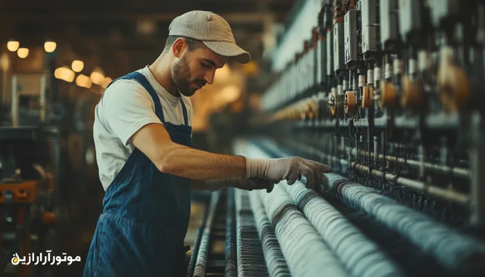 تکنسین کارخانه نساجی در حال بررسی عملکرد دوکهای ریسندگی در خط تولید نخ – نمایی از دقت و مهارت در تنظیم ماشینآلات صنعتی سبک