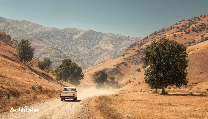 خودروی وانت سفید در جاده خاکی و تپهای درهشهر زیر آفتاب تابستان، گردوغبار و تلالو نور خورشید در چشمانداز خشک و کوهستانی. روغن موتور درهشهر